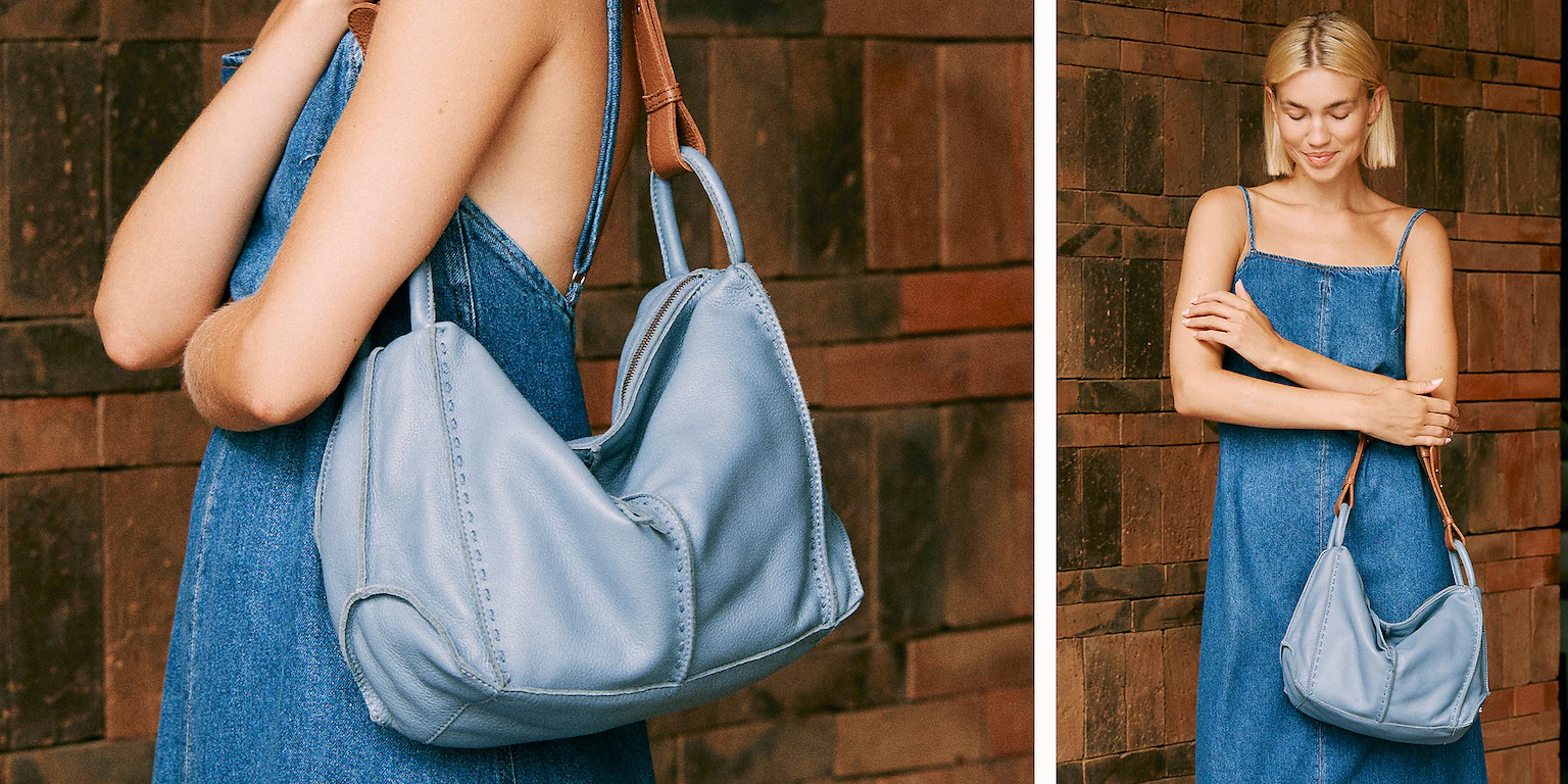 Woman in blue dress holding large blue bag, brick wall background