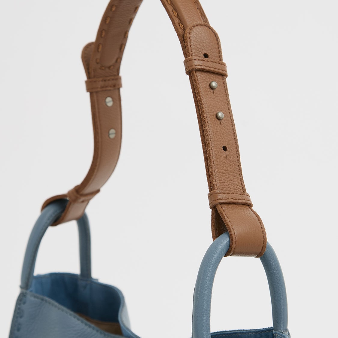 A close-up of a beige and blue handbag with a brown strap and adjustable buckle
