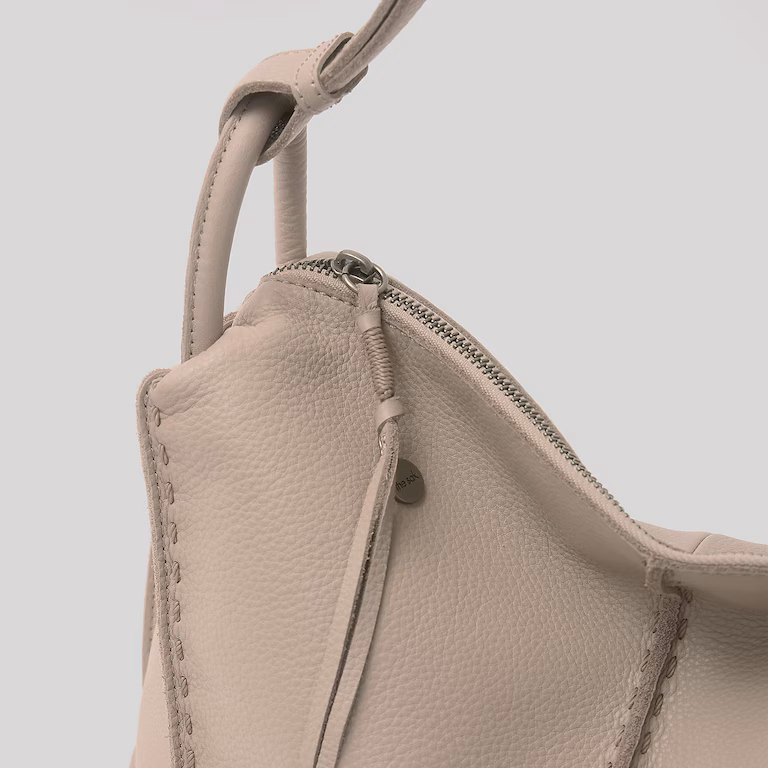 Close-up of a beige leather bag with visible stitching and zipper
