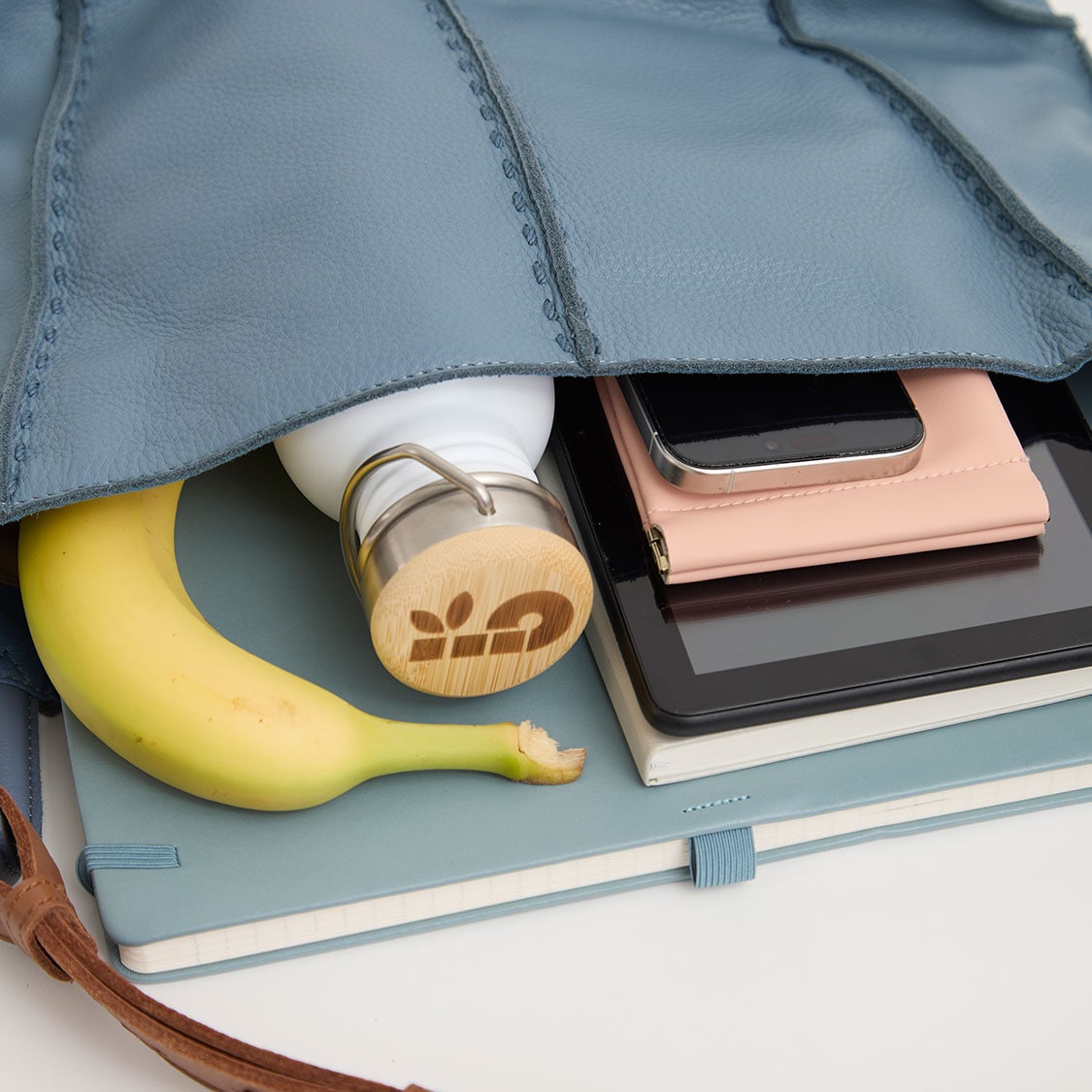 Travel essentials including a banana, headphones, phone, notebook, and passport inside a blue bag
