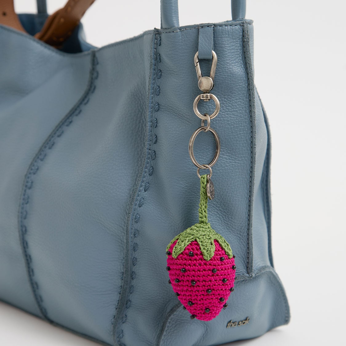 Keychain with pink and green strawberry charm hanging from a blue bag