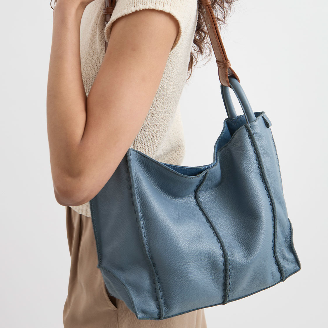 A woman carries a large blue tote bag over her shoulder